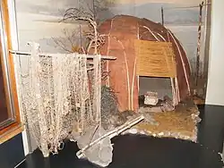 Летнее нанайское жилище из бересты и ивовых прутьев. На заднем плане&nbsp;— вешала́ для ю́колы, спереди&nbsp;— рыбацкие сети и деревянный якорь.Хабаровский краевой музей имени Н. И. Гродекова