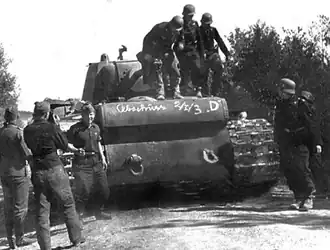 Немецкие военнослужащие осматривают «расейняйский КВ», 25 июня 1941 года. Как указывает М.&nbsp;В.&nbsp;Коломиец, надпись на корпусе танка свидетельствует о том, что он был уничтожен расчётом орудия D 2-й батареи 1-го дивизиона 3-го зенитного полка