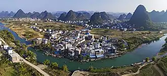 Посёлок Юйлунцунь. Слева по центру — мост Юйлунцяо через реку Юйлунхэ, построенный во времена династии Мин. Холмы за посёлком — карстовые останцы буферной зоны Южно-Китайского карста