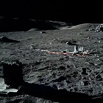 Приборы ALSEP. На переднем плане слева&nbsp;— радиоизотопный термоэлектрогенератор. Левее центра&nbsp;— прибор, регистрирующий частоту падения метеоритов. Правее центра&nbsp;— куча мусора из упаковок. У правого края снимка и чуть выше центра&nbsp;— геофонный модуль. Выше него&nbsp;— скала Geophone Rock. Левее неё&nbsp;— красный флажок в месте размещения одного из геофонов