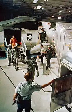 Экипаж «Аполлона-11» на борту авианосца «Хорнет» переходит из вертолёта в карантинный фургон. Впереди&nbsp;— Коллинз, за ним&nbsp;— Армстронг и Олдрин