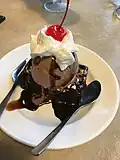 Взбитые сливки с пирожным брауни, коктейльной вишней и шариком мороженого.