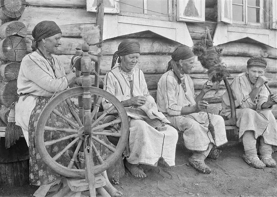 Женщины, прядут у стены дома.