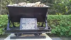 Вагонетка со сланцем на постаменте. Русскоязычная часть надписи на памятнике: Здесь в июне 1916 года была добыта первая партия сланца для промышленных цели