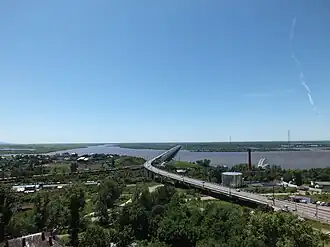 Хабаровский мост в июле 2013 года. Амур течёт слева направо, выше моста в него впадает Пемзенская протока. Также видны поезда на станции Амур.