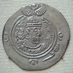 A silver coin with a face of Khosrau II surrounded by a double ring and some symbols