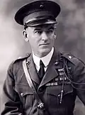 A black and white image of Logan Feland, a white male in his Marine Corps Service A uniform. He is wearing a hat several ribbons and a Fourragère. He also has a leather strap from his right shoulder to his left waist.