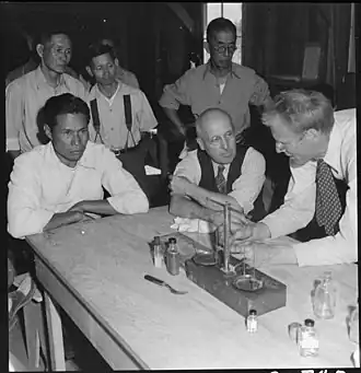 Роберт Эмерсон (справа) объясняет процесс получения резины из гваюла директору проекта Рою Нэшу (слева) на фоне депортированных японцев (Манзанар, Калифорния).