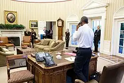 13 июля 2015 года в Овальном кабинете (стоит возле часов) при разговоре Обамы с госсекретарём Джоном Керри о подписании соглашения о ядерной программе Ирана.
