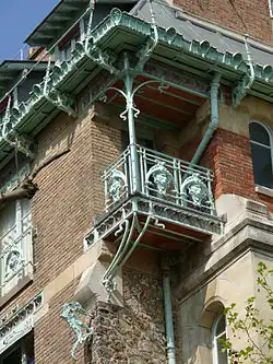 Цветная фотография угла здания с разнообразными материалами и орнаментами из светлого кованого железа, сине-зеленого оттенка