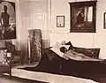 Naked youth poses prone in the Villa Lysis of Capri, where Nino Cesarini lived with his protector and lover, the Baron Jacques d'Adelswärd-Fersen. The photograph was taken by Wilhelm von Plüschow and the portrait of Cesarini is visible on the wall.
