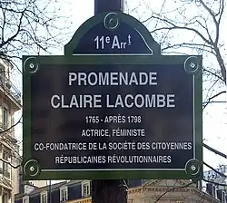 Табличка на столбе с надписью: 11 e Ar t — PROMENADE CLAIRE LACOMBE — 1765 – APRĖS 1798 —  ACTRICE, FÉMINISTE, CO-FONDATRICE DE LA SOCIÉTÉ DES CITOYENNES RÉPUBLICAINS RÉVOLUTIONNAIRES