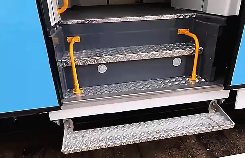 Открытая выдвижная ступенька и две стационарные внутренние ступени тамбура. На нижней внутренней ступени видны лампы освещения