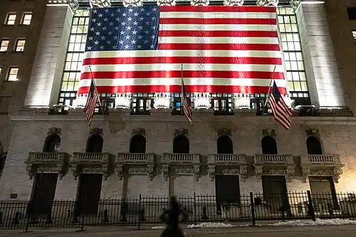 Статуя (тёмный силуэт внизу) лицом к зданию NYSE в феврале 2019